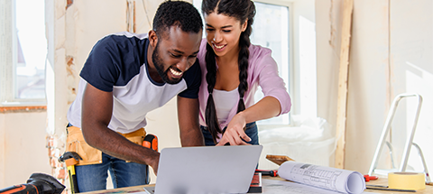 couple looking at laptop in house under construction