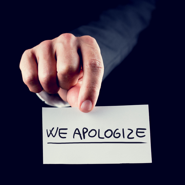 person holding up paper that says "we apologize"