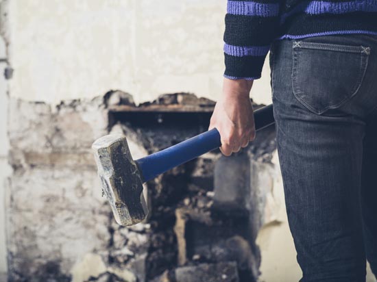 person holding sledgehammer facing wall