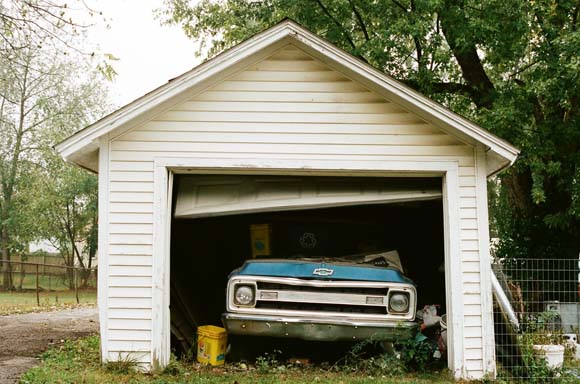 old garage with broken door and run-down truck parked inside