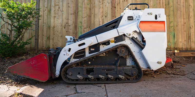 Bobcat machine working on cracked and broken up concrete driveway