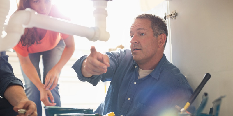 repairman working on plumbing under sink