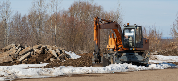 excavator breaking up snow covered concrete parking lot