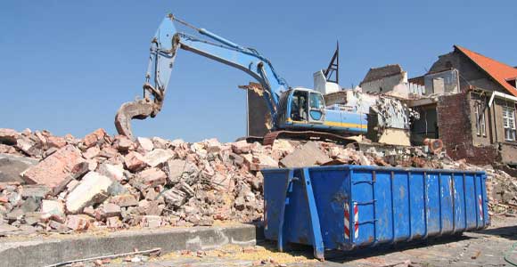 excavator loading concrete into dumpster at demolition site