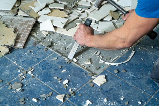 person using mallet and chisel to remove floor tiles